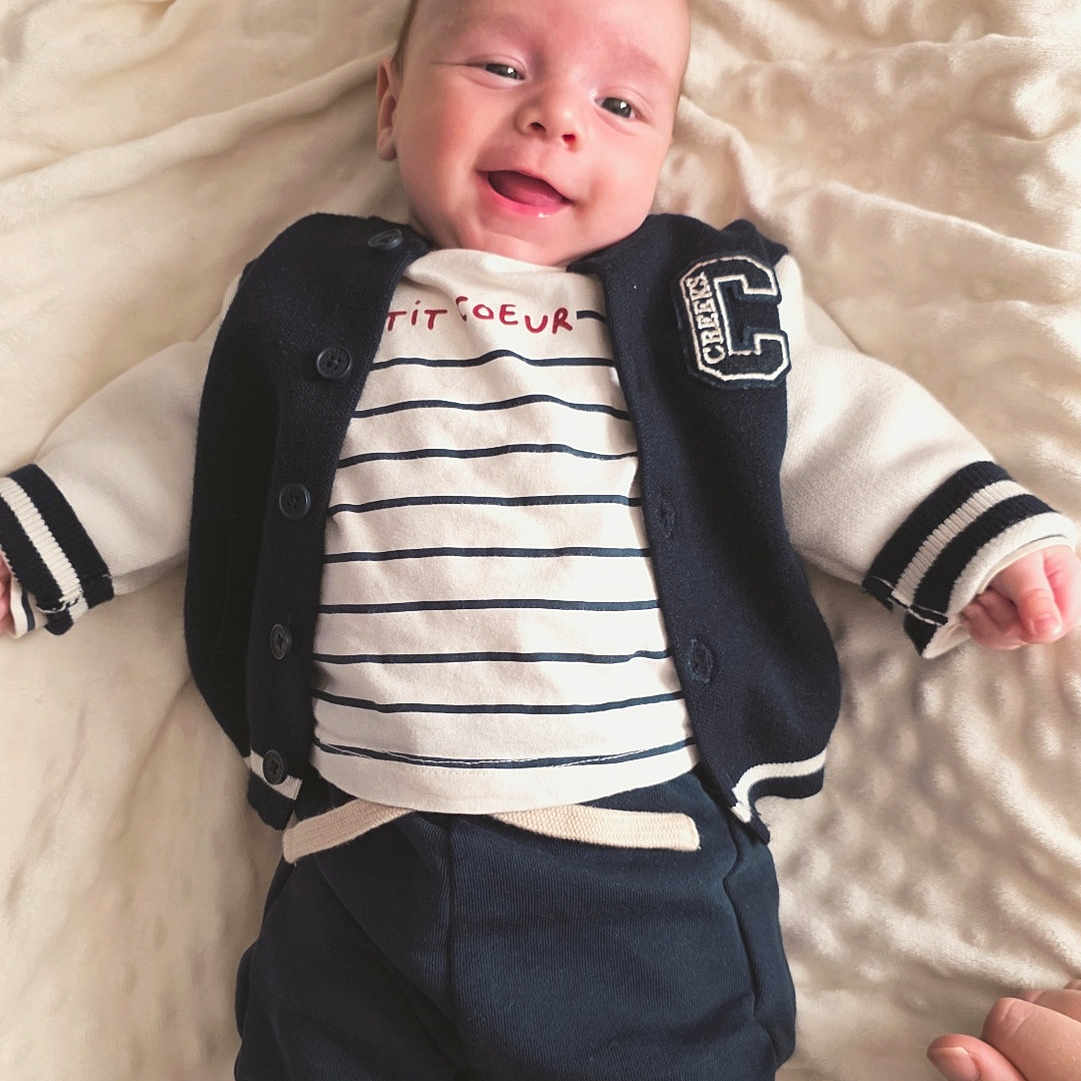 Eden participe au concours pour gagner de l'argent avec cette photo : baby, blanket, child, clothing, comfortable, cozy, cute, hand, happy, indoors, infant, lying_down, navy_jacket, pants, person, portrait, smiling, socks, soft_texture, striped_shirt