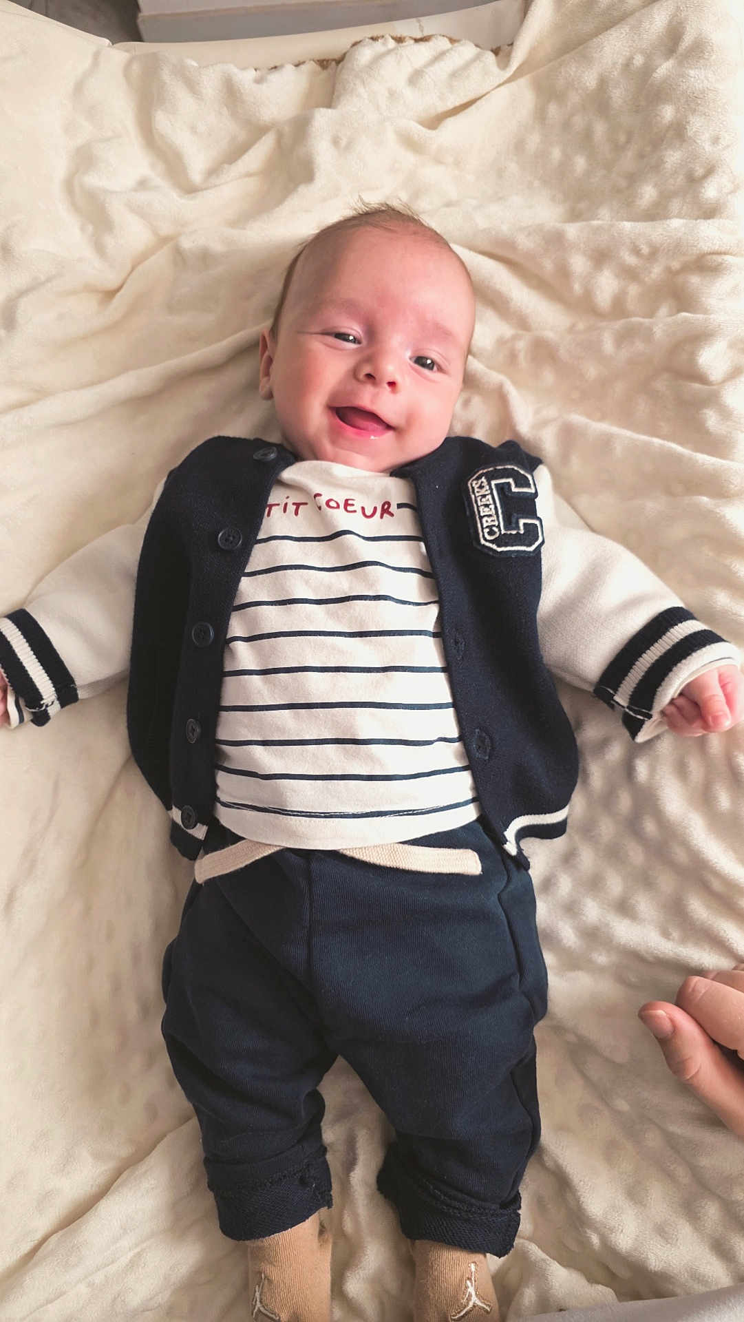 Eden participe au concours pour gagner de l'argent avec cette photo : baby, infant, smiling, blanket, clothing, navy_jacket, striped_shirt, pants, socks, lying_down, happy, cute, portrait, child, soft_texture, hand, indoors, cozy, comfortable, person