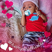 Angelo is registered to the contest to win money with this photo: baby, blanket, blue_dinosaur, camo_pants, child, closeup, cute, hashtag, hat, hearts, indoors, infant, love, lying_down, pacifier, patterned_clothing, portrait, red_shirt, soft_texture, text_overlay