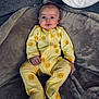 baby, infant, onesie, yellow_clothing, sun_pattern, blanket, soft_texture, indoor, couch, seated, portrait, child, cute, smiling, face, hand, foot, comfort, cozy, relaxed