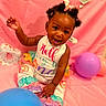 baby, child, smiling, sitting, balloon, pink_background, colorful_clothing, bows, cute, happy, celebration, one_year, portrait, indoor, playful, infant, ruffled_pants, bright_colors, person, fun