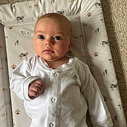 Evelyn joined the competition — help win amazing prizes! baby, infant, onesie, white_clothing, face, blue_eyes, hand, cushioned_pad, animal_print, cow_pattern, tree_pattern, carpet, indoor, child, cute, portrait, newborn, lying_down, curious, soft_lighting