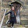 black_dress, black_jacket, casual_clothing, child, daylight, fashion, girl, happy, long_hair, outdoor, playful, portrait, railing, smile, sneakers, standing, steps, stone_wall, wooden_door, young_person