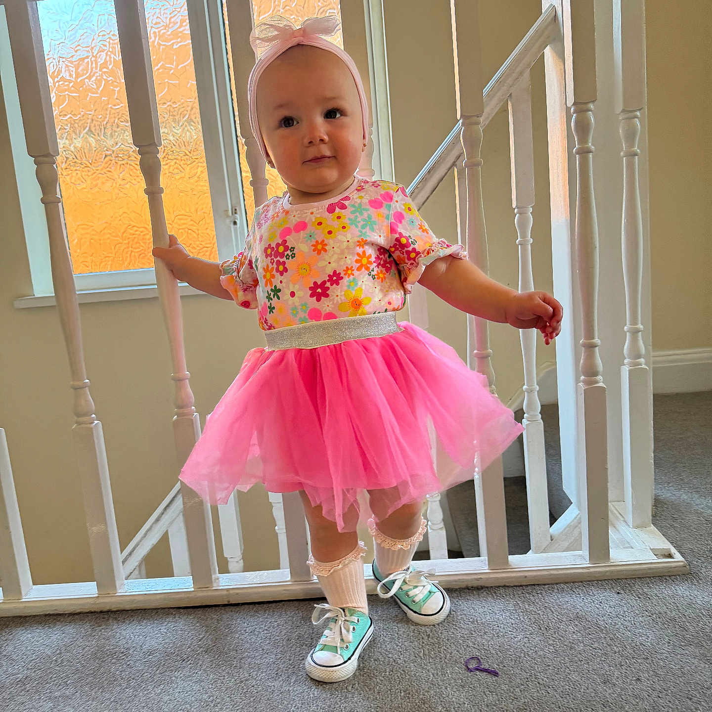 Jasmine is registered to the contest to win money with this photo: toddler, child, pink_tutu, floral_top, headband, sneakers, indoor, carpet, banister, staircase, window, natural_light, cute, portrait, smiling, playful, fashion, young_child, person, home