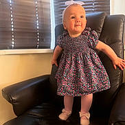 Jasmine is registered to the contest to win money with this photo: baby, child, girl, standing, dress, floral_pattern, headband, bow, tights, shoes, chair, leather, window, blinds, indoor, happy, cute, portrait, person, smiling