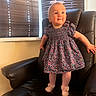 baby, child, girl, standing, dress, floral_pattern, headband, bow, tights, shoes, chair, leather, window, blinds, indoor, happy, cute, portrait, person, smiling
