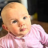 Jasmine is registered to the contest to win money with this photo: baby, child, face, portrait, pink_clothing, curious, indoor, cute, infant, soft_light, closeup, small_ears, buttoned_shirt, human, young_child, eyelashes, skin, head, expression, adorable