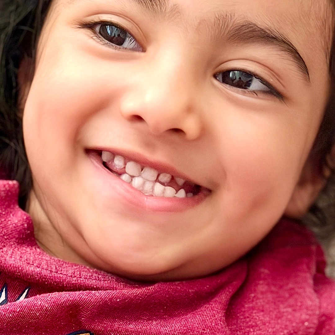 Iknoor is registered to the contest to win money with this photo: cheerful, child, close_up, clothing, colorful, eyes, face, hair, happy, head, indoors, person, photograph, pink_shirt, portrait, selfie, smiling, teeth, toothy_grin, young