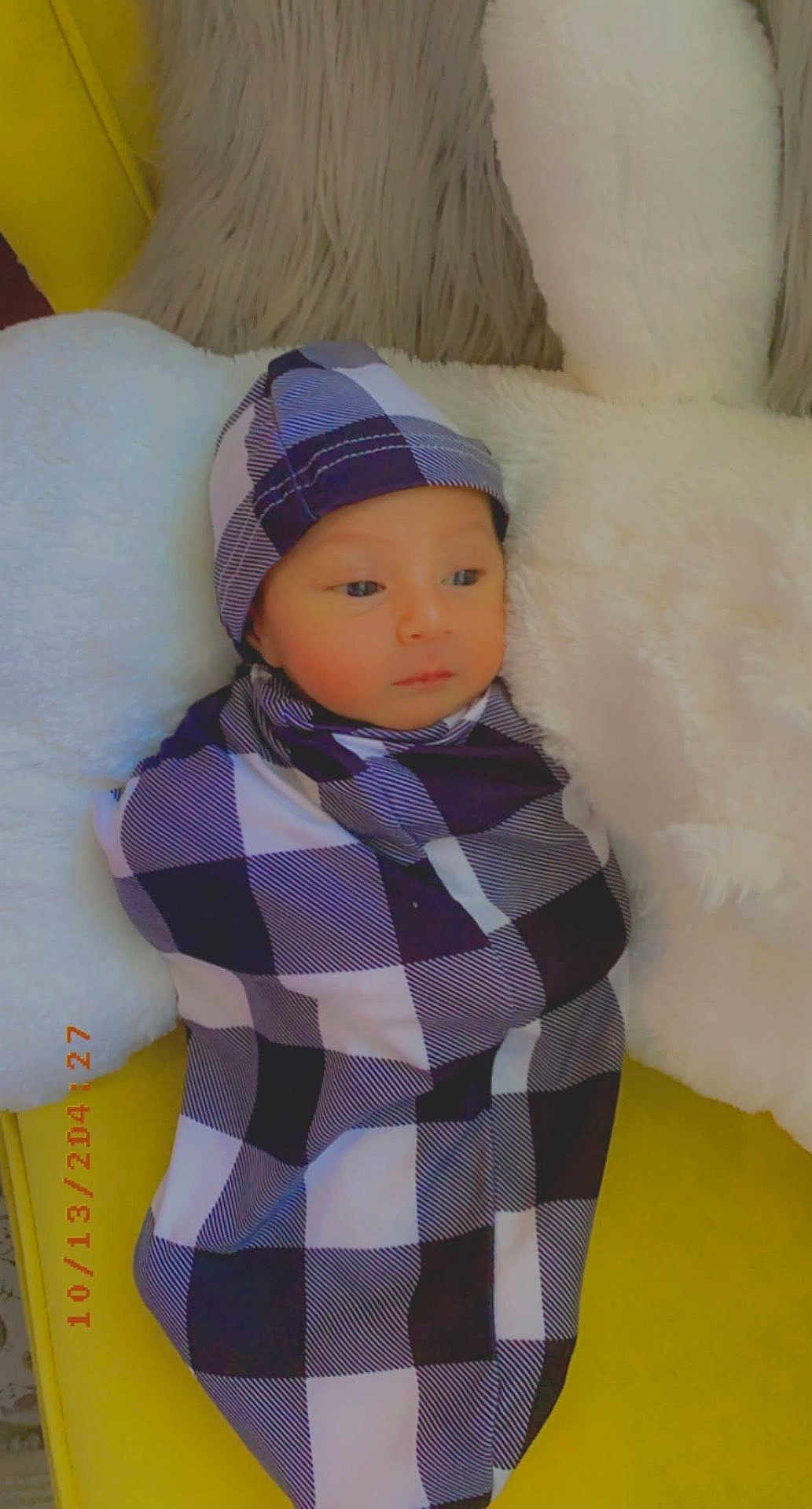 Jad joined the competition — help win amazing prizes! baby, child, infant, wrapped, blanket, checkered_pattern, hat, pillow, soft_texture, yellow_background, indoors, portrait, cute, sleepy, resting, cozy, clothing, newborn, face, person