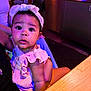 Ramiya is registered to the contest to win money with this photo: baby, child, indoor, headband, pink_clothing, curious, person, seated, table, arm, jewelry, lighting, colorful_lights, face, portrait, infant, cute, ruffles, skin, expression