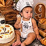 baby, child, infant, chef_hat, apron, bakery, bread, cake, birthday, nine_months, flour, spoon, sitting, portrait, food, pastry, indoor, smiling, decor, photography