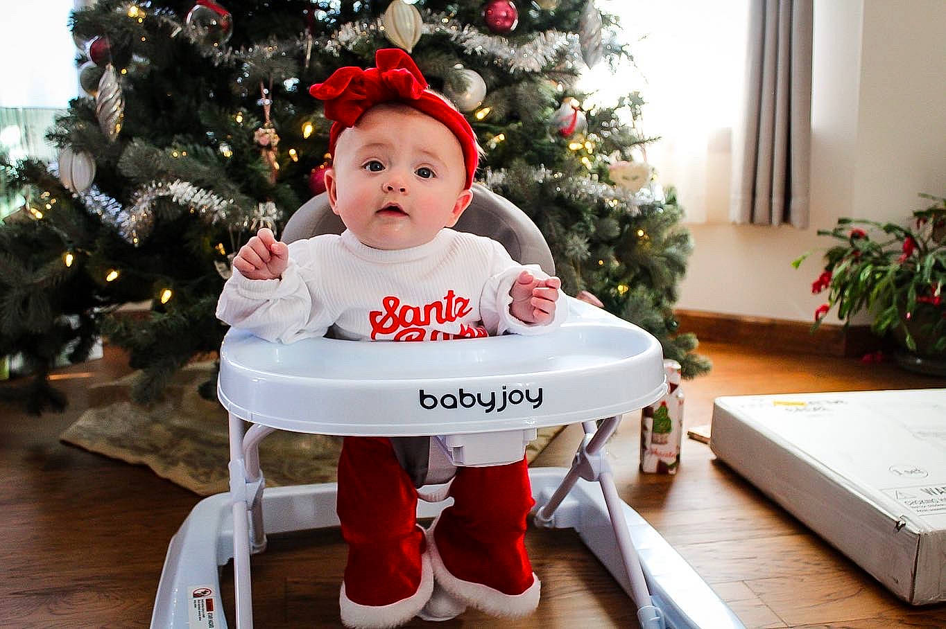 Eliana is registered to the contest to win money with this photo: baby, baby_toddler_clothing, child, christmas_decoration, christmas_ornament, christmas_tree, dress, event, happy, holiday, holiday_ornament, human_body, ornament, outerwear, person, plant, red, sleeve, toddler, tree