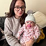 Areleigh is registered to the contest to win money with this photo: baby, child, comfort, couch, cushion, face, glasses, holding, indoor, knit_hat, long_hair, onesie, pacifier, person, polka_dot, pom_pom, portrait, seated, sweater, woman