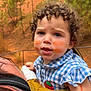 Maddy a rejoint le concours — aidez-le/la à gagner de superbes lots ! toddler, child, curly_hair, paint_smudges, baby_carrier, outdoor, nature, trees, red_soil, blue_checkered_shirt, face, expression, person, closeup, infant, summer, daylight, skin, cute, portrait