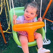 Maddy participe au concours pour gagner de l'argent avec cette photo : toddler, child, swing, green_swing, orange_handle, garden, grass, curly_hair, white_shoes, playground, outdoor, rope, happy, smiling, striped_clothing, person, baby, daylight, fun, seat