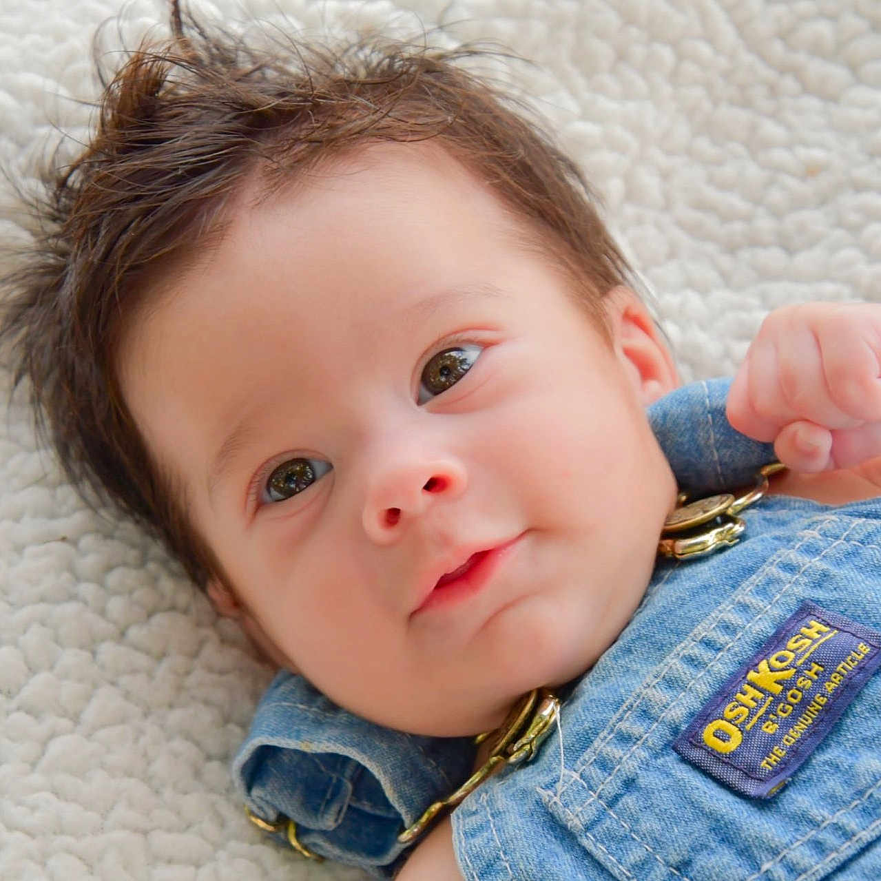 Braxton is registered to the contest to win money with this photo: baby, child, closeup, clothing, cute, denim_overalls, expression, eyes, face, hair, hand, indoors, infant, lying_down, newborn, portrait, skin, smile, soft_blanket, young_child