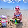 Hina a rejoint le concours — aidez-le/la à gagner de superbes lots ! child, girl, beach, sand, toys, bucket, cap, sunny, sky, clouds, playing, summer, sandcastle, smiling, barefoot, necklace, outdoor, vacation, holiday, fun