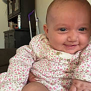 Lydia Rose is registered to the contest to win money with this photo: baby, smiling, infant, onesie, floral_pattern, hand, furniture, cabinet, portrait, home_interior, diaper, skin, face, person, child, cute, happy, closeup, seated, indoor