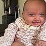 baby, smiling, infant, onesie, floral_pattern, hand, furniture, cabinet, portrait, home_interior, diaper, skin, face, person, child, cute, happy, closeup, seated, indoor