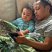 Kane joined the competition — help win amazing prizes! baby, blanket, casual, child, couch, cozy, curly_hair, family, gray_shirt, holding, home, indoor, looking, natural_light, phone, portrait, relaxing, siblings, striped_shirt, togetherness