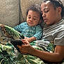 baby, blanket, casual, child, couch, cozy, curly_hair, family, gray_shirt, holding, home, indoor, looking, natural_light, phone, portrait, relaxing, siblings, striped_shirt, togetherness