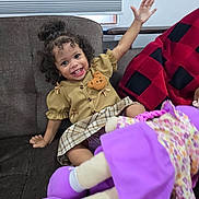 Valeria joined the competition — help win amazing prizes! toddler, child, smiling, curly_hair, couch, indoor, toy, doll, purple, plaid_skirt, bear_patch, waving, happy, person, clothing, window_blind, blanket, red_black, hair_bun, playful