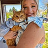 woman, cat, outdoor, smiling, blue_sky, trees, porch, dress, orange_cat, pet, happy, holding, sunlight, nature, greenery, face, closeup, daylight, fashion, animal