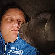 Sally joined the competition — help win amazing prizes! person, dog, face, sleeping, affection, close_up, blue_jacket, zip_up, indoor, dark_background, pet, companion, resting, cozy, nuzzling, animal, friendship, head, portrait, casual