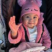 Rhian joined the competition — help win amazing prizes! baby, child, pink_hat, pom_poms, jacket, blanket, stroller, smile, waving_hand, cute, warm_clothing, infant, outdoor, face, happy, person, portrait, baby_clothes, cozy, toddler