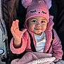 baby, child, pink_hat, pom_poms, jacket, blanket, stroller, smile, waving_hand, cute, warm_clothing, infant, outdoor, face, happy, person, portrait, baby_clothes, cozy, toddler