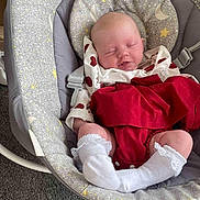 Aurora is registered to the contest to win money with this photo: baby, infant, sleeping, baby_rocker, clothing, socks, red_dress, white_socks, face, head, cute, indoor, soft_toys, pattern, stars, moon, carpet, comfort, rest, peaceful