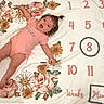 baby, child, infant, portrait, lying_down, smiling, happy, floral_blanket, milestone_blanket, week_eight, flowers, daisies, roses, sunflowers, pink_outfit, onesie, indoor, closeup, calendar, celebration