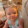 baby, child, toddler, portrait, face, eyes, blonde_hair, hair_bows, flower_hair_accessories, sleeveless_top, blue_clothing, sitting, indoors, home, couch, soft_lighting, close_up, looking_at_camera, calm_expression, photography