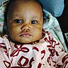 Izzabelle is registered to the contest to win money with this photo: baby, infant, child, portrait, face, eyes, wide_eyed, serious_expression, pink_outfit, patterned_clothing, bows, blanket, bedding, indoors, close_up, sitting, lying_down, dark_hair, brown_skin, photography