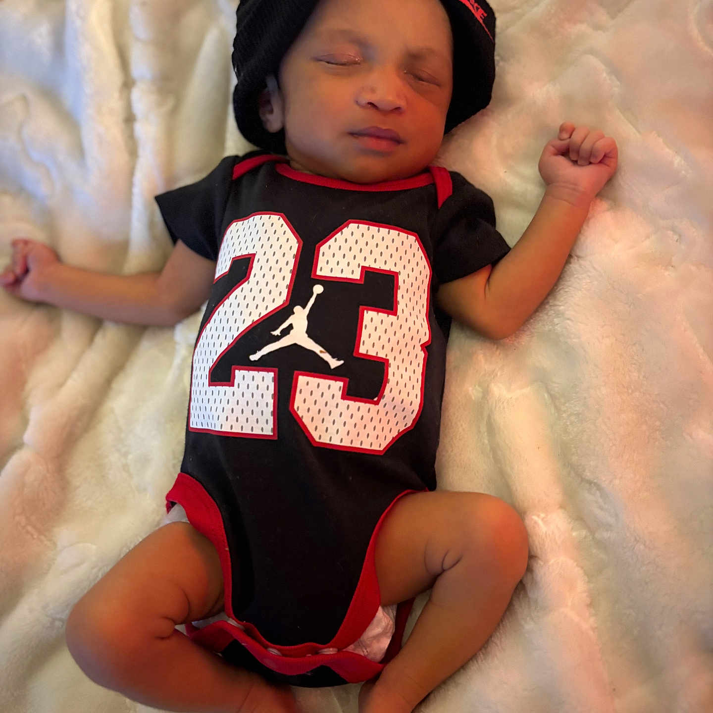 Terrion is registered to the contest to win money with this photo: baby, sleeping, infant, onesie, black_clothing, red_trim, number_23, beanie, hat, blanket, soft_texture, cozy, indoor, resting, cute, peaceful, small, child, portrait, human