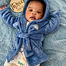 baby, infant, blue_robe, hood, blanket, wooden_sign, three_months, dinosaur_pajamas, cute, lying_down, face, child, cozy, soft_texture, indoors, portrait, smiling, clothing, person, newborn