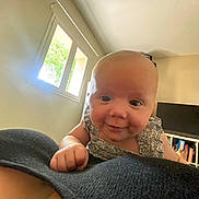 Léna a rejoint le concours — aidez-le/la à gagner de superbes lots ! baby, bookshelf, child, clothing, couch, curious, cute, face, furniture, hand, head, home, indoor, living_room, person, portrait, skin, smiling, television, window