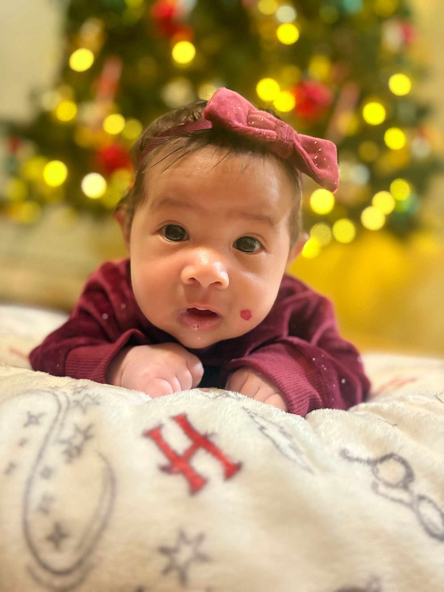 Carla joined the competition — help win amazing prizes! baby, infant, face, headband, bow, sweater, blanket, christmas_tree, bokeh, holiday, indoors, cute, portrait, child, young, lying_down, expression, soft_focus, warm_lighting, festive