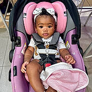Joy is registered to the contest to win money with this photo: baby, infant, car_seat, pink, headband, blanket, white_sandal, floor, tile, child, seat_belt, curly_hair, indoor, person, cute, clothing, sitting, toy, footwear, child_safety