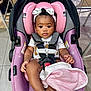 baby, infant, car_seat, pink, headband, blanket, white_sandal, floor, tile, child, seat_belt, curly_hair, indoor, person, cute, clothing, sitting, toy, footwear, child_safety