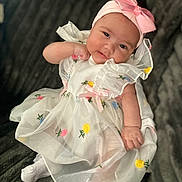 Remi is registered to the contest to win money with this photo: baby, child, smiling, dress, headband, bow, flower_embroidery, white_clothing, infant, cute, soft_blanket, lying_down, portrait, happy, indoors, closeup, baby_girl, toddler, people, childhood