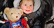 Elizabeth joined the competition — help win amazing prizes! baby, child, cozy, cute, daylight, face, happy, hood, infant, jacket, outdoor, pavement, person, plush_toy, protective_cover, smile, stroller, teddy_bear, toy, warm_clothing