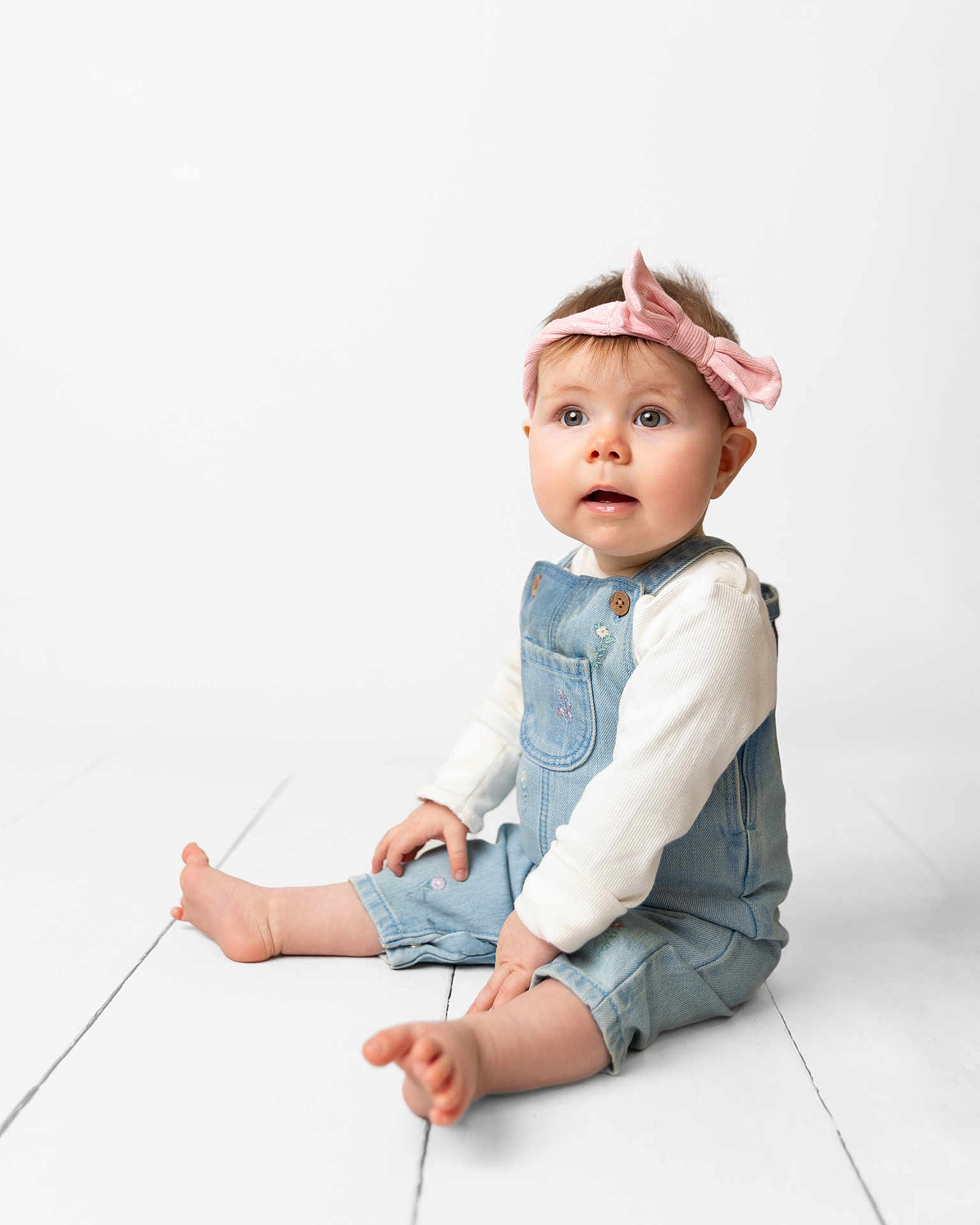Elizabeth joined the competition — help win amazing prizes! baby, barefoot, bright, child, curious, cute, denim_overalls, floor, girl, headband, indoor, infant, innocent, pink_bow, portrait, sitting, studio, white_shirt, wooden_floor, young