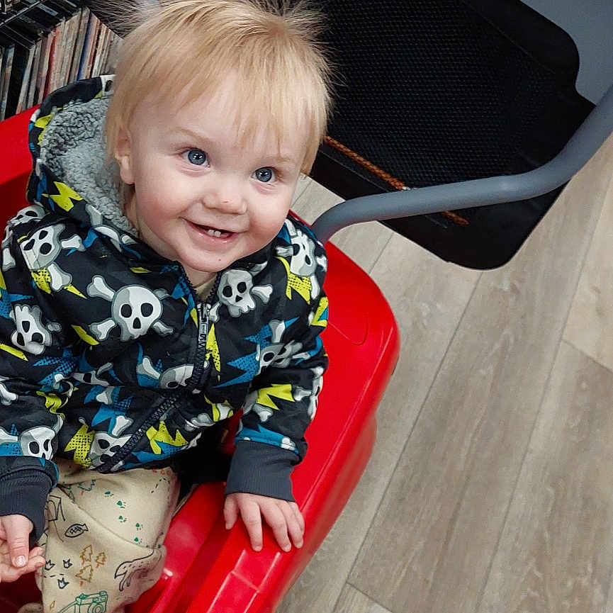 Bowen is registered to the contest to win money with this photo: baby, book, bookcase, clothing, dress, face, footwear, furniture, head, indoors, library, pants, person, photography, playarea, portrait, publication, shelf, shoe, wood