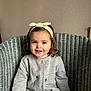Julianna participe au concours pour gagner de l'argent avec cette photo : toddler, child, smiling, headband, curly_hair, cardigan, gray_clothing, sitting, wicker_chair, indoor, person, happy, cute, portrait, young_child, fashion, cozy, casual, female, relaxed