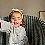 toddler, child, smiling, happy, curly_hair, headband, sweater, embroidered, chair, woven_chair, indoor, person, portrait, cute, baby, hand, seated, cozy, warm_clothing, playful