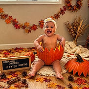 Lorraine joined the competition — help win amazing prizes! baby, child, infant, smiling, laughing, portrait, pumpkin, autumn, fall, harvest, leaves, seasonal_decor, headband, indoors, wooden_floor, crochet_blanket, wreath, letterboard, sitting, cozy