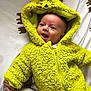 baby, child, hoodie, yellow_clothing, grinch, smiling, face, infant, bed, blanket, pattern, animal_print, happy, cute, warm_clothing, zipped_jacket, lying_down, soft_texture, portrait, cozy