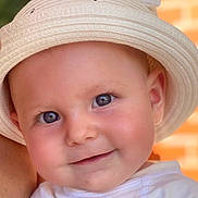 Anaëlle participe au concours pour gagner de l'argent avec cette photo : baby, child, face, hat, smile, blue_eyes, skin, white_clothing, closeup, portrait, cheeks, infant, cute, headwear, person, young_child, warm_light, indoors, expression, happy
