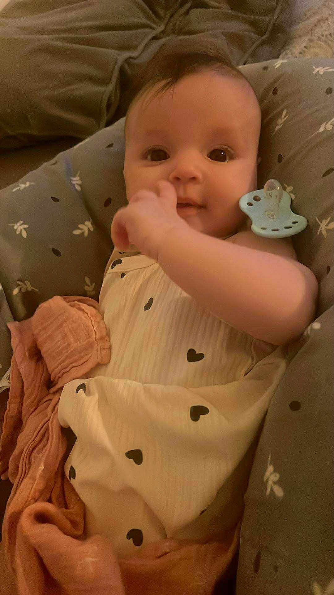 Janna a rejoint le concours — aidez-le/la à gagner de superbes lots ! baby, infant, pacifier, blanket, cushion, clothing, heart_pattern, hand, face, person, cute, indoor, soft_lighting, comfort, resting, child, expression, looking, newborn, seat